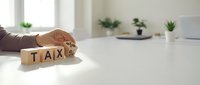 Unrecognizable person holding wooden blocks spelling tax on white desk in bright office space, representing tax planning and financial management concepts.