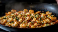 Juicy grilled shrimp with garlic and fresh herbs in black pan, close up view. Seafood cooked with parsley and butter sauce, mediterranean cuisine preparation.