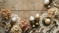 Easter table setting with eggs in vintage holders, dried hydrangea flowers, lace doilies and antique cutlery on rustic wooden background for spring holiday.