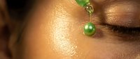 Close-up of African American woman's face with green pearl jewelry accent highlighting natural glowing skin texture and closed eyes for beauty skincare concept.