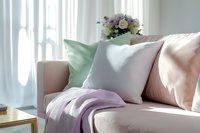 Cozy sofa corner with soft pastel pillows and throw blanket near sunlit window, fresh flowers in vase creating serene home atmosphere for interior design and decor.
