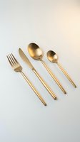 Matte gold cutlery set with fork, knife, and two spoons on a light background, elegant flatware for modern table settings.