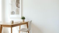 Minimalist home office with wooden desk, white chair, small plant, and abstract wall art in a bright, clean interior space.