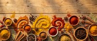 Colorful spices and seasonings arranged in wooden bowls and spoons on rustic wood background. Cooking ingredients including turmeric, paprika, cinnamon sticks.