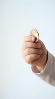 Hand holding golden coin between fingers on neutral background for finance and investment concepts.