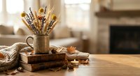 Cozy autumn home decor with dried flowers in ceramic vase, candles, books and warm blanket on wooden table creating hygge atmosphere for seasonal interior design.