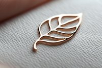 Elegant rose gold leaf shaped metal pin on textured white leather background, minimalist nature-inspired jewelry design for branding and luxury accessories.