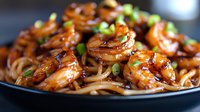 Stir fried shrimp with noodles in sweet and savory Asian sauce garnished with fresh green onions, served on black plate with glazed caramelized coating.