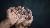 Two hands holding a clear glass sphere with swirling light trails inside, symbolizing energy, innovation, and future technology concepts.