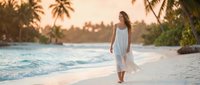 Young woman in white dress walking on tropical beach at sunset with palm trees and turquoise water creating peaceful vacation atmosphere.