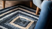 Geometric knitted blanket in navy blue and beige tones with diamond pattern texture, cozy home decor detail with modern Scandinavian style armchair visible in background.