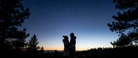 Adult male holding young child against starry night sky with forest silhouettes, capturing wonder and bonding moments for family, parenting, and outdoor lifestyle content.