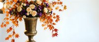 Elegant autumn floral arrangement in brass vase with orange maple leaves, roses and berries for seasonal home decor and thanksgiving celebrations.