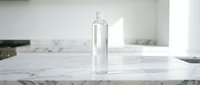 Clear glass bottle with dropper cap on white marble countertop in bright minimalist kitchen setting, suitable for cosmetics, skincare, essential oils, and product packaging design.
