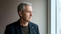 Senior man with gray hair and light skin tone wearing dark blazer and gray shirt, looking thoughtfully to the side in professional portrait setting for business, corporate, and lifestyle use.