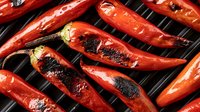 Grilled red chili peppers with charred marks on barbecue grill, showcasing vibrant color and smoky texture for spicy cuisine preparation.