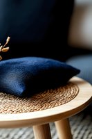 Navy blue cushion on woven rattan placemat atop wooden stool, creating minimalist home decor composition with natural textures and modern styling.