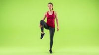 Young athletic woman in red tank top performing high knee exercise on green background for fitness training and workout routines.