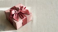 Pink gift box with elegant satin ribbon bow on neutral linen background for special occasions, holidays, birthdays, anniversaries and celebration moments.