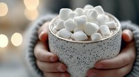 Cozy ceramic mug filled with hot chocolate and mini marshmallows held in hands against blurred bokeh lights background, creating warm winter mood.