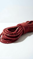 Coiled red climbing rope with weathered texture on white background, suitable for adventure sports, safety equipment, and outdoor recreation concepts.