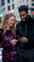 Happy interracial couple laughing while looking at smartphones together on city street. Young Caucasian woman and African American man sharing social media content outdoors.