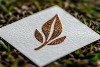 Elegant copper foil leaf logo mockup on textured white paper against natural grass background, showcasing minimalist eco-friendly branding design.
