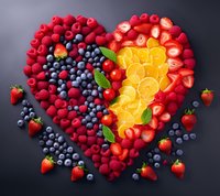 Fresh heart shape made of mixed berries, orange slices and mint leaves arranged on dark background, romantic healthy food concept for Valentine's day celebration.