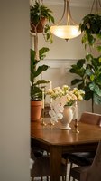 Cozy dining room interior with wooden table, pendant light, fresh flowers in vase, hanging plants and warm ambient lighting for home decor inspiration.