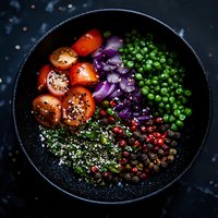 Fresh colorful vegetables and seeds in black bowl on dark background - cherry tomatoes, red onion, green peas, pomegranate, hemp seeds arranged in sections.