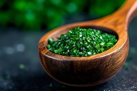 Fresh chopped parsley in wooden spoon on dark background with selective focus, macro food photography for cooking and culinary blogs.