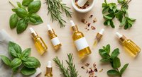 Natural essential oil bottles with fresh herbs including basil, rosemary and oregano on wooden background for aromatherapy and wellness applications.