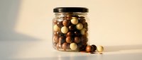 Glass jar filled with mixed colorful olives on white surface with warm natural lighting for gourmet food photography and culinary design projects.