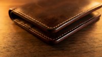 Brown leather wallet with stitched edges on wooden surface showcasing craftsmanship and quality materials for business and personal use.