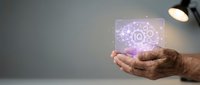 Mature male hand holding glowing tablet displaying artificial intelligence and gear icons, representing digital innovation and technology solutions for business applications.