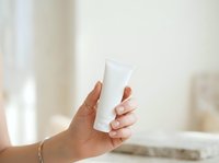 Unbranded white cosmetic tube held in hand against neutral background, suitable for skincare, sunscreen, lotion, or cream product mockups and packaging design.