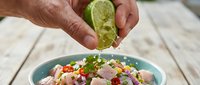 Close-up of hands squeezing fresh lime juice over colorful ceviche with seafood, vegetables and citrus. Food preparation and cooking concept.