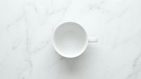 Empty white ceramic cup on marble surface, overhead view, isolated on white background for design, branding, and product mockup use.