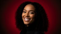 Young African American woman with curly hair smiling confidently against red background for professional headshot and business portrait photography.