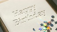Elegant embossed Happy Birthday card with holographic star confetti on cream textured paper, celebrating a special occasion in style.