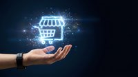 Hand holding glowing neon shopping cart icon with digital particles and light effects on dark background for e-commerce and online retail concepts.