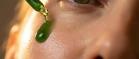 Fresh green jade roller massaging woman's face during skincare routine for anti-aging and wellness treatment in natural sunlight.
