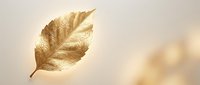 Golden metallic leaf floating against soft beige background with warm bokeh lights. Luxury autumn concept for elegant design projects and seasonal decorations.