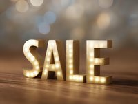 Illuminated SALE text with glowing LED lights on wooden surface against blurred bokeh background, creating warm atmospheric retail display.