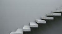 Modern concrete floating staircase against minimalist gray wall showcasing contemporary architectural design and clean geometric lines for interior spaces.