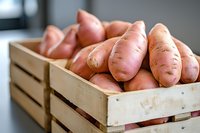 Fresh organic sweet potatoes in wooden crate, close up view of raw root vegetables with rustic texture and natural pink skin, farm harvest produce.