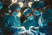 Surgical team of Asian medical professionals performing operation in hospital operating room with dramatic lighting and teal color scheme.