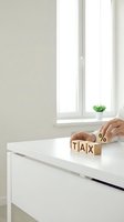 Businesswoman arranging wooden blocks spelling tax with percentage symbol on white desk by bright window, representing accounting, financial planning, and tax preparation services.