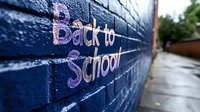 Back to school chalk text on blue brick wall with shallow depth of field for educational marketing and student preparation campaigns.
