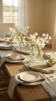 Rustic wooden dining table set with neutral tableware and white spring flowers in glass vases creating warm natural home decor atmosphere.